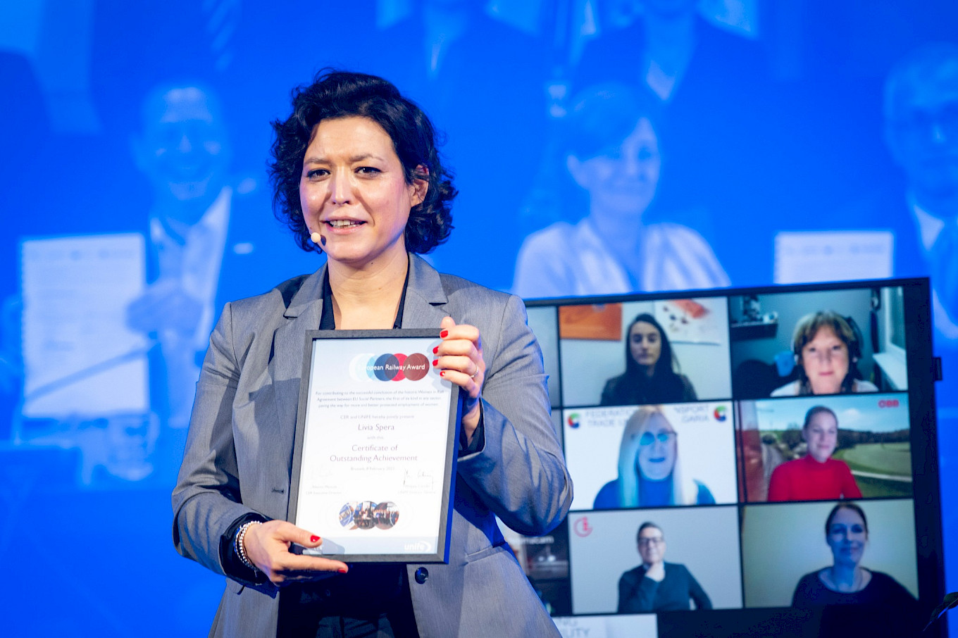 ETF-Generalsekretärin Livia Spera mit Auszeichnungsurkunde. Auf dem Bildschirm im Hintergrund Mitglieder der ETF-Verhandlungsdelegation.