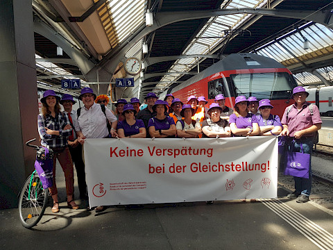 SEV-Aktion in Z&uuml;rich f&uuml;r Lohn- und Einkommensgleichheit: Das Einkommen der Frauen liegt in der Schweiz durchschnittlich 43,2% unter demjenigen der M&auml;nner (Bundesamt f&uuml;r Statistik, 2022). Dies wegen Lohnunterschieden, weil die Frauen in schlecht bezahlten Stellen &uuml;bervertreten und in gut bezahlten unterverteten sind und weil sie mehr unbezahlte Care-Arbeit leisten als die M&auml;nner und darum weniger Zeit haben f&uuml;r bezahlte Arbeit. Umgerechnet auf einen achtst&uuml;ndigen Arbeitstag (8-12/13-17) betr&auml;gt der Unterschied 3 Std. 27 Min. Das heisst: Die Frauen arbeiten ab 13.33 Uhr gratis! Damit liegt die Schweiz bei der Einkommensgleichheit auf Rang 28 von 30 europ&auml;ischen L&auml;ndern.